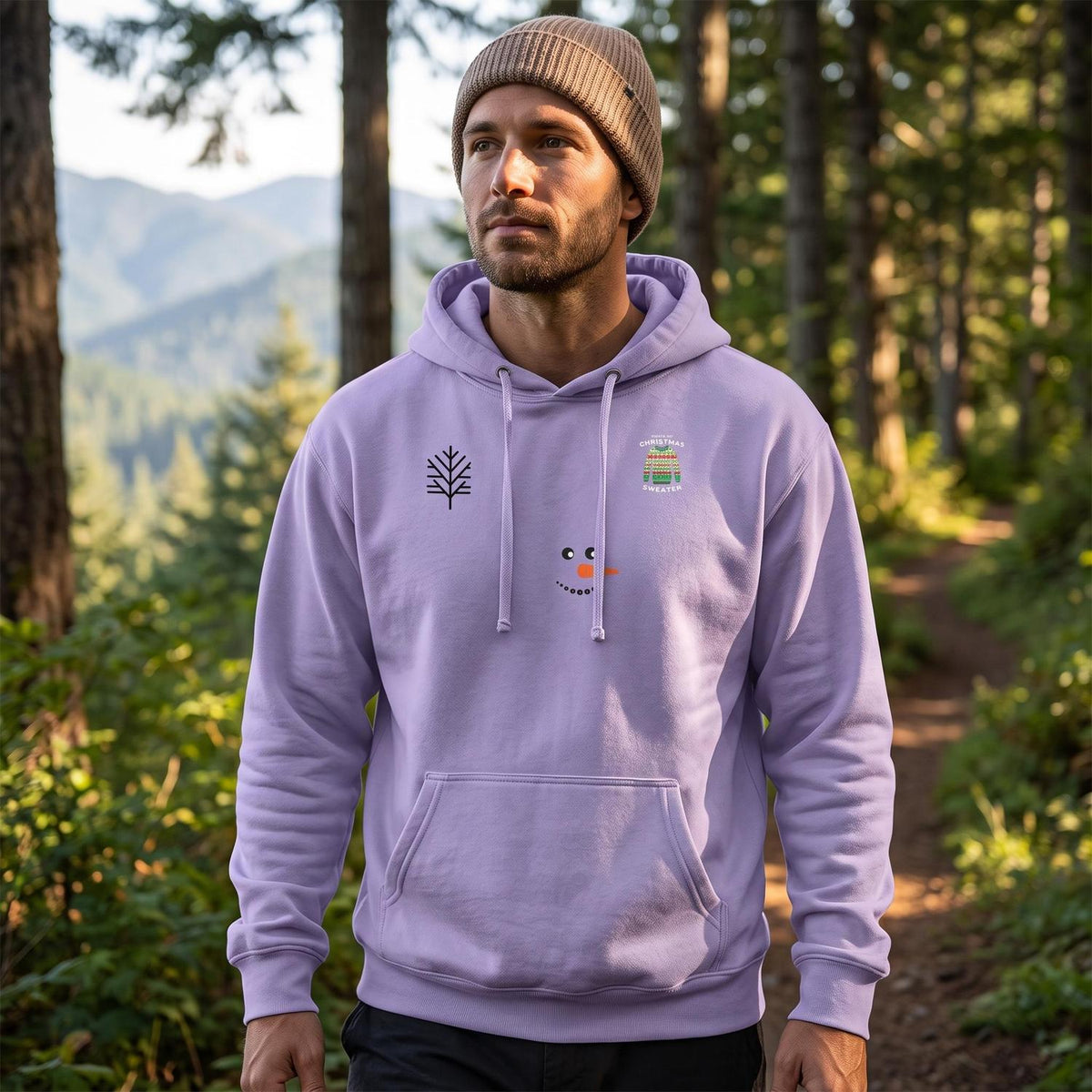 Man wearing a lavender pullover hoodie with tree and snowman graphics on a wooded trail.