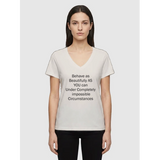 Woman wearing off white V-neck affirmation T-shirt with text Behave as Beautifully as You Can Under Completely Impossible Circumstances, Le Van Kamp Studio